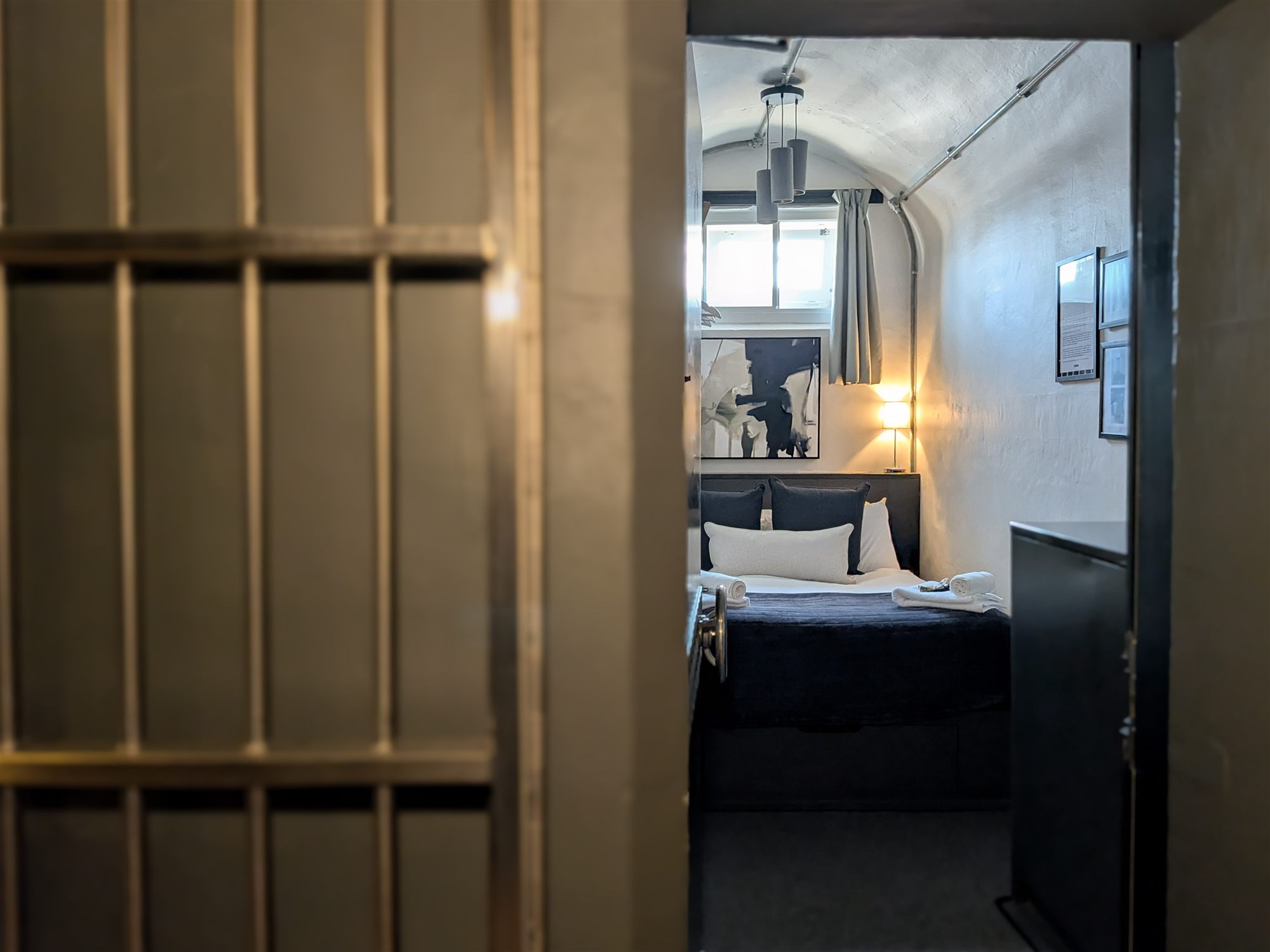 A Private Cell bedroom seen through an original barred jail cell door at CODE The Court